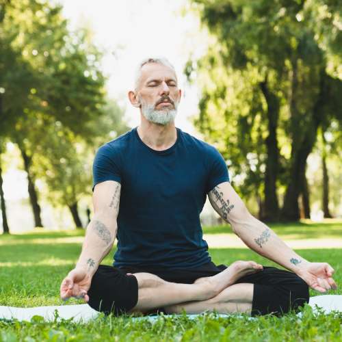 Man meditating on green grass yoga mat concentrating on his breathing exercises